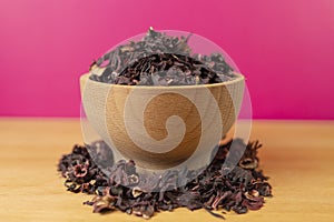 Dry hibiscus tea  in bowl on wooden board. purple background behind. herb. herbal tea. food ingredient