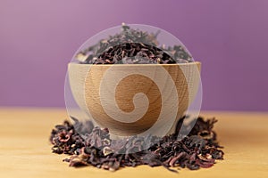 Dry hibiscus tea  in bowl on wooden board. violet background behind. herb. herbal tea. food ingredient