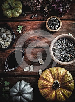 Dry hydrangea, pumpkins, pumpkin oil and seeds in wooden bowls on wood table