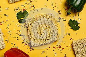 Dry instant noodle block with seasonings on yellow background