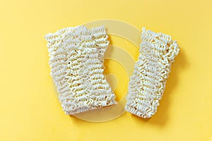 Dry instant noodles broken in two on yellow background, copy space