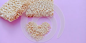 Dry instant noodles with heart shape on pink background.