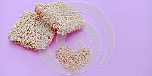 Dry instant noodles with heart shape on pink background.