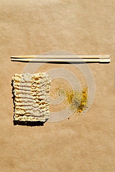 Dry instant noodles with wooden chopsticks and seasoning over brown background. photo
