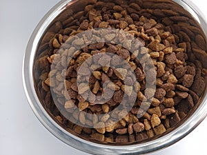 Dry kibble dog food on a metal bowl on a white background