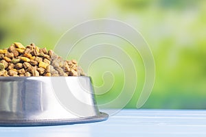 Dry kibble pet food in bowl. Dog or cat food on garden table