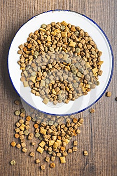 Dry kibble pet food. Dog or cat food in bowl on wooden table. Top view