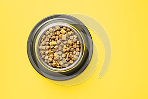 Dry kibble pet food. Dog or cat food in bowl on yellow background. Top view