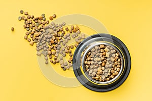 Dry kibble pet food. Dog or cat food in bowl on yellow background. Top view