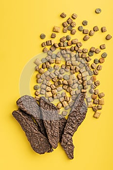 Dry kibble pet food and dry meat. Dog or cat food on yellow background. Top view