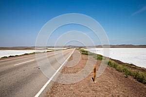 Dry lake salt flags on summer road with white lane under cloudy sky