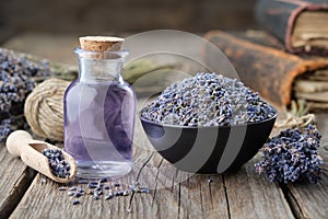 Dry lavender flowers in bowl and bottle of essential lavender oil or infused water. Old books and lavender flowers on background.