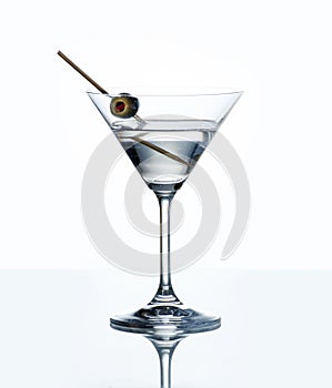 Dry martini with green olive in cocktail glass over white background with reflection.