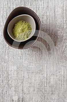 Dry Matcha tea in a small brown plate. Grey wood background. Top