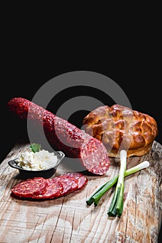 Dry meat sausage on a wooden plate with vegetables