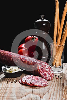 Dry meat sausage on a wooden plate with vegetables