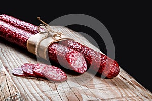 Dry meat sausage on a wooden plate with vegetables