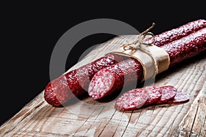 Dry meat sausage on a wooden plate with vegetables