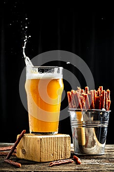 Dry Mini salami sticks with cold craft light beer in a glass with water drops. Dried snacks for beer