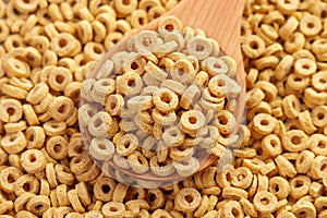 Dry oat flake rings in wooden spoonful. Pile of crispy round oatmeal cereals