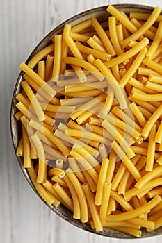 Dry Organic Maccheroni Pasta in a Bowl on a white wooden surface, top view. Flat lay, overhead, from above. Close-up