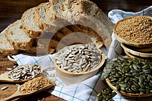 Dry organic sunflower seeds in wooden bowl over blur whole wheat bread, golden flax and pumpkin seed