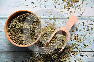 Dry parsley in a wooden bowl with a wooden measuring spoon on a wooden table. photo