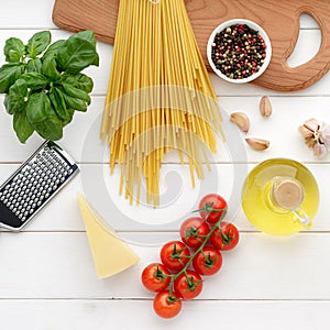Dry pasta bucatini or spaghetti with basil, oil, cheese, tomatoes on white wooden background.