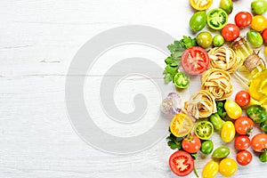 Dry pasta, tomatoes, greens, oil and ingredients. Italian traditional cuisine. Fresh vegetables. Top view.