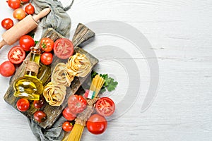 Dry pasta, tomatoes, greens, oil and ingredients. Italian traditional cuisine. Fresh vegetables. Top view.