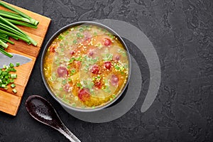 Dry Yellow Pea Soup with meat sausages, potato, green onions and sesame in black bowl at dark slate background