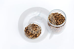 Dry pet food in a glass jar and bowl close-up on a white background. View from above