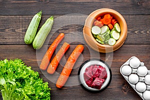 Dry pet food with natural ingredients. Raw meat, vegetables zucchini and carrot near eggs on dark wooden backgroud top