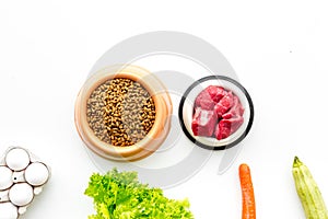 Dry pet food with natural ingredients. Raw meat, vegetables zucchini and carrot near eggs on white backgroud top view