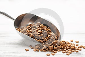 Dry pet food in scoop on white wooden background