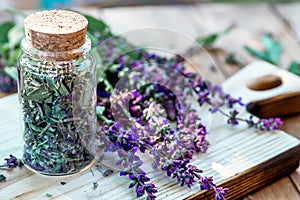 Dry purple sage flowers in a glass jar with a cortical lid. A sage plant on a wooden cutting board. preparation of medicinal herbs