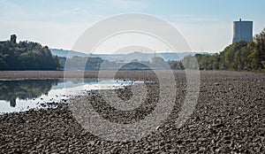 Dry riverbed with stones, visible chimney of a nuclear power plant.