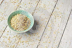 Dry rolled oatmeal in bowl on white wooden background. Top view.