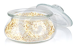 Dry rolled oats in a open transparent glass oval storage jar with glass lid isolated on white background