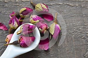 Dry rose buds flowers in a white spoon on old wooden table.Asian ingredient for aromatherapy herbal tea.