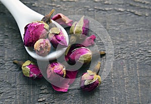 Dry rose buds flowers in a white spoon on old wooden table.Asian ingredient for aromatherapy herbal tea.