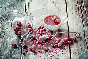 Dry rose buds, tea cup, strainer and glass jar with rosebuds.