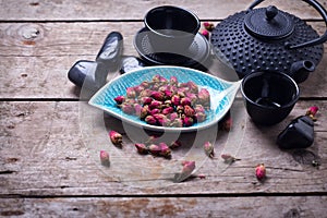 Dry rose tea in bowl and traditional asian tea set on aged woo