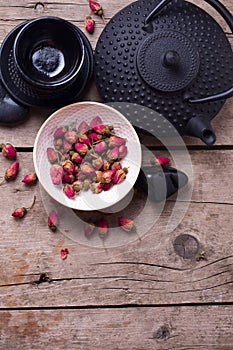 Dry rose tea in bowl and traditional asian tea set on aged woo