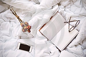 Dry roses, smartphone and vintage notebook on bed