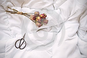 Dry roses and vintage scissors on bed