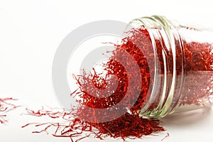 Dry saffron threads in a glass jar scattered on a white background photo