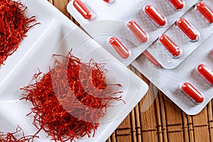 Dry saffron threads and pills in blister on a wooden background photo