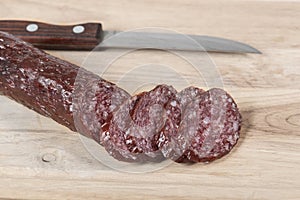 Dry salami sausage and knife on wooden board with slices