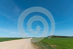 A dry sandy road passes through a field under the scorching sun and clouds. Dirt road outside the city in the village. Arid